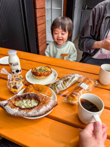 那須での家族旅行中に屋外テラスで楽しんだ朝食風景|笑顔の子どもと美味しいパン・コーヒー・地元牛乳が並ぶ春の朝のひととき